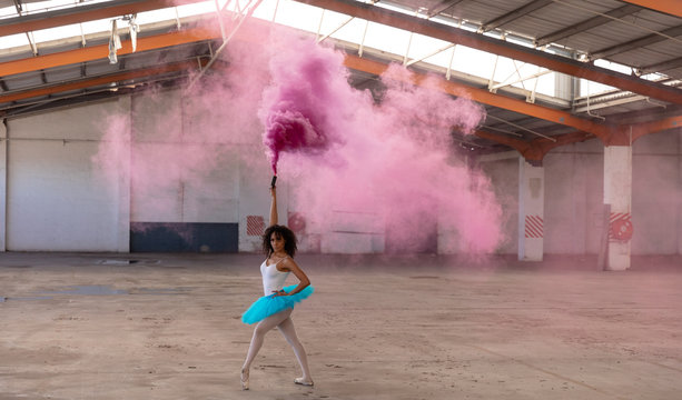 Female dancer in an empty warehouse holding smoke grenade