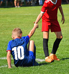 Young kid soccer player helps on the field - obrazy, fototapety, plakaty