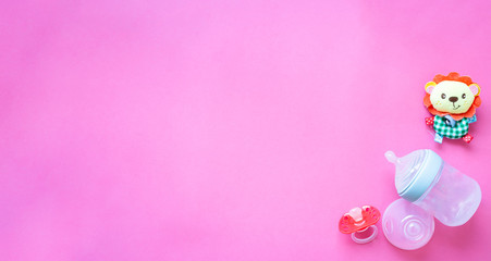 Baby accessories and toys on pink background. Pacifier and feeding bottle.