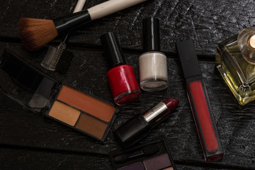 Various cosmetics on a black background (nail polish, eye shadow palette, lipstick, brush). Close up photo.