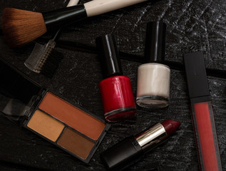 Various cosmetics on a black background (nail polish, eye shadow palette, lipstick, brush). Close up photo.