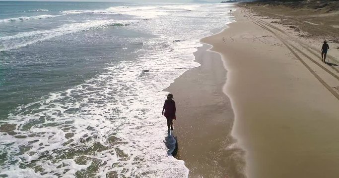 Dron vuela sobre Joven con traje de ba&ntilde;o paseando en costa dorada