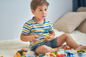 happy asian boy playing with colorful construction plastic blocks on white Bed at home.