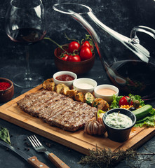 Fried steak on a wooden stand with baked potatoes and vegetables