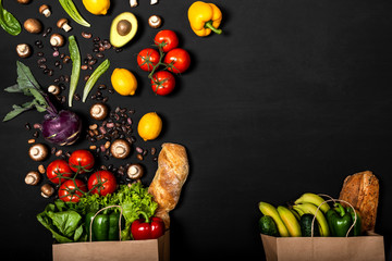 Two shopping paper bags full of different fresh vegetables and bread on a black background. Purchases concept. Healthy food organic selection. Top view, copy space