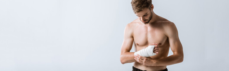 Obraz premium panoramic shot of shirtless sportsman with elastic bandage on wrist isolated on grey