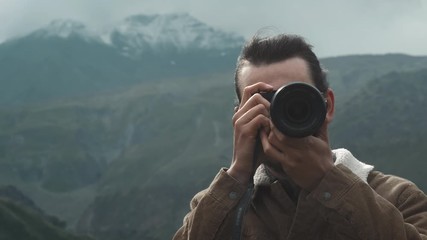 PORTTAIT: Male traveler photographer makes professional mountains pictures for blog. A guy with long hair and a beard holding a professional camera in his hands. Expedition to the mountains