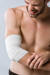 Naklejka premium partial view of shirtless sportsman with elastic bandage on elbow isolated on grey