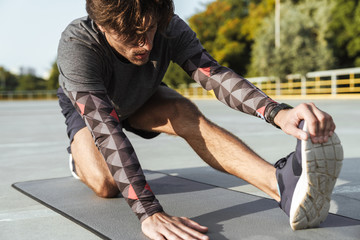 Fototapeta na wymiar Photo of athletic unshaven man stretching his leg on mat
