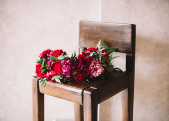 Fototapeta na wymiar Beautiful blossoming burgundy colored peonies and roses head wreath on the rustic wooden chair, minimalistic view