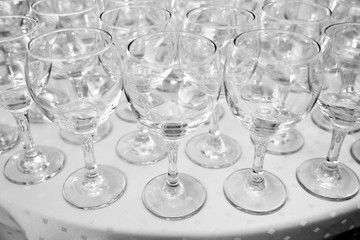 Empty clean glasses standing in a row on a table prepared by the bartender for champagne and wine. Several of transparent glasses on a rack. Catering for the event. A lot of wine glasses in a row .