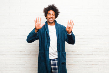young black man wearing pajamas with gown smiling and looking friendly, showing number nine or...