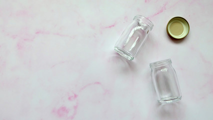 Flat lay of two empty glass bottles and lid, on a pink surface. 