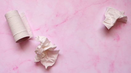 White crumpled tissue paper and toilet paper roll on a pink marble background.
