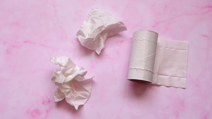 White crumpled tissue paper and toilet paper roll on a pink marble background.