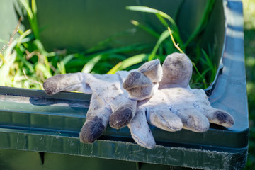 Green bin container filled with garden waste. Dirty gardening gloves. Spring clean up in the garden. Recycling garbage for a better environment.