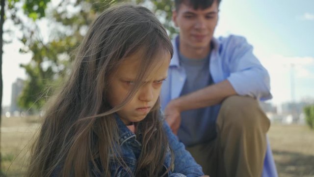 Portrait of childly offended and angry little harm girl on the background of her elder brother in sunny autumn day.