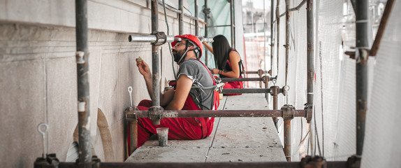 Two workers on the scaffolding, plastering and renovating old building