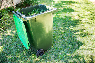 Green bin container filled with garden waste. Spring clean up in the garden. Recycling garbage for a better environment.