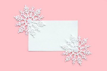 White paper card decorated with snowflakes on pink background. New Year, Christmas and winter concept. Flat lay, top view, free copy space.