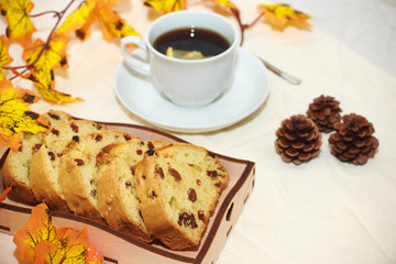 Autumn layout. A cup of black tea with lemon. Baking on a round white saucer and fir cones.