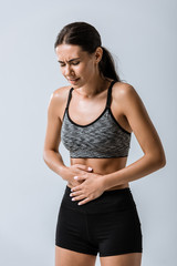 attractive sportswoman with stomach pain isolated on grey