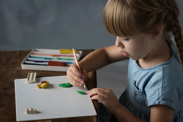 a little girl sculpts from plasticine sitting at the table