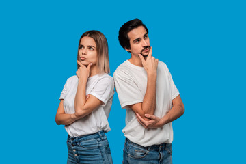 Thoughtful bearded brunet man with mustache and blond woman in white t-shirts and blue jeands standing isolated over white background. Concept of conversation and thinking.