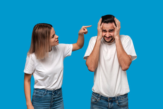 Young blond woman and brunet bearded man with mustaches in white t-shirts and blue jeans quarreling standing isolated over blue background. Concept of relationship crisis.