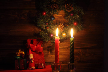 Two candles with Christmas decorations and toy Santa in dark interior