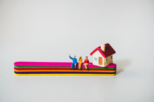 Miniature people, man and woman sitting on popsicle stick with mini house
