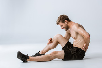 shirtless bearded sportsman with lower back pain on grey