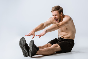 shirtless bearded man in black sneakers stretching on grey