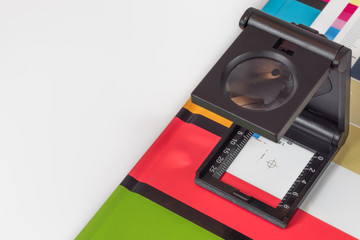 Black magnifying  glass standing on  the test print with colored background. Print loupe on offset printed sheet with basic colors control bars.