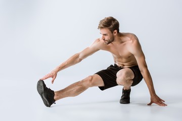 shirtless bearded man in black sneakers stretching on grey