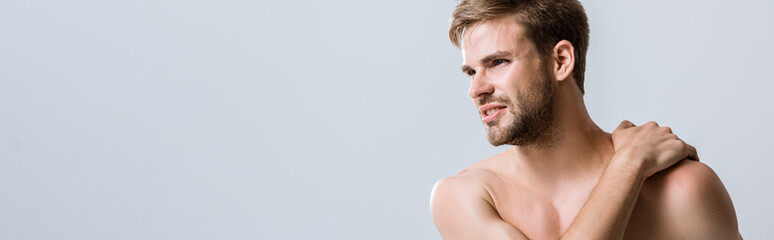 Fototapeta premium panoramic shot of shirtless bearded man with pain in shoulder isolated on grey