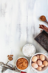 Empty vintage bread loaf pan with pumpkin puree, flour, cinnamon and brown eggs over light rustic background. Pumpkin bread recipe. Image shot from top view.