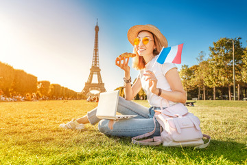 Happy Asian girl with French flag eating croissant and learning foreign languages on laptop with...