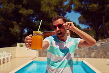 Attractive man drinking juice on the swimming pool. Summer concept.