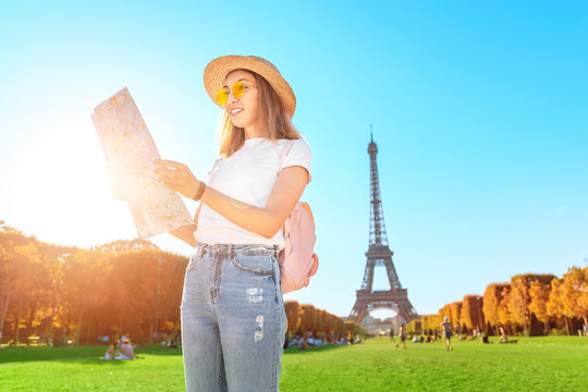 Happy asian woman reading map in front of the famous Paris landmark - Eiffel tower. Tourism in France