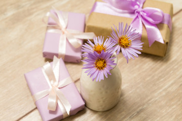 Purple spring flowers in a white vase on a wooden table. Gift box wrapped in craft paper with ribbon