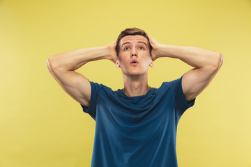 Fototapeta na wymiar Caucasian young man's half-length portrait on yellow studio background. Beautiful male model in blue shirt. Concept of human emotions, facial expression. Looking up, looks shocked, astonished.