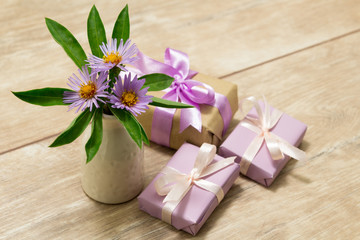Obraz na płótnie Canvas Purple spring flowers in a white vase on a wooden table. Gift box wrapped in craft paper with ribbon