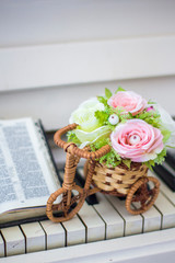 Decorative flowers (roses) in a wicker bicycle on the piano and the Bible. Topiary. Wedding decor, decoration. Close-up.