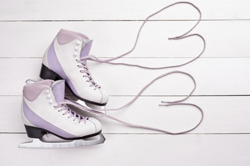 Close-up photo of professional ice skates lying on a white wooden background.