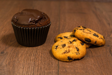 Chocolate muffin and shortbread cookies on a brown wooden surface.
