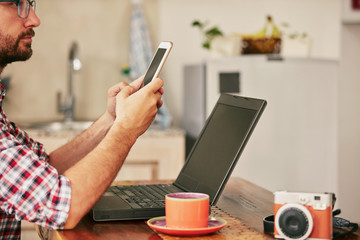 Modern bearded man using cellphone and drinking coffee with laptop.