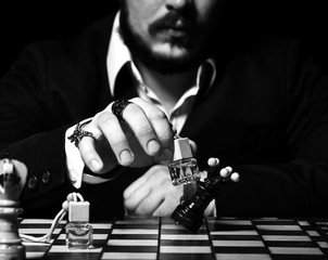 Brutal man in official suit and stylish rings playing chess with bottle of perfume, making a move, attack black queen
