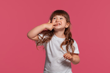 Close-up portrait of a little brunette girl dressed in a white t-shirt posing against a pink studio...