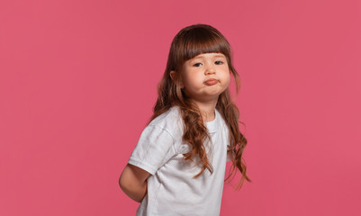 Fototapeta premium Close-up portrait of a little brunette girl dressed in a white t-shirt posing against a pink studio background. Sincere emotions concept.